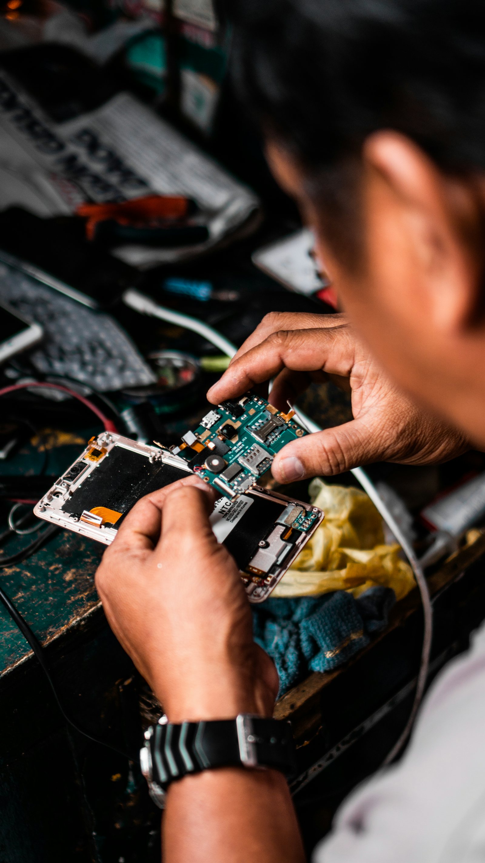 A technician working on the circuit board of an opened smartphone